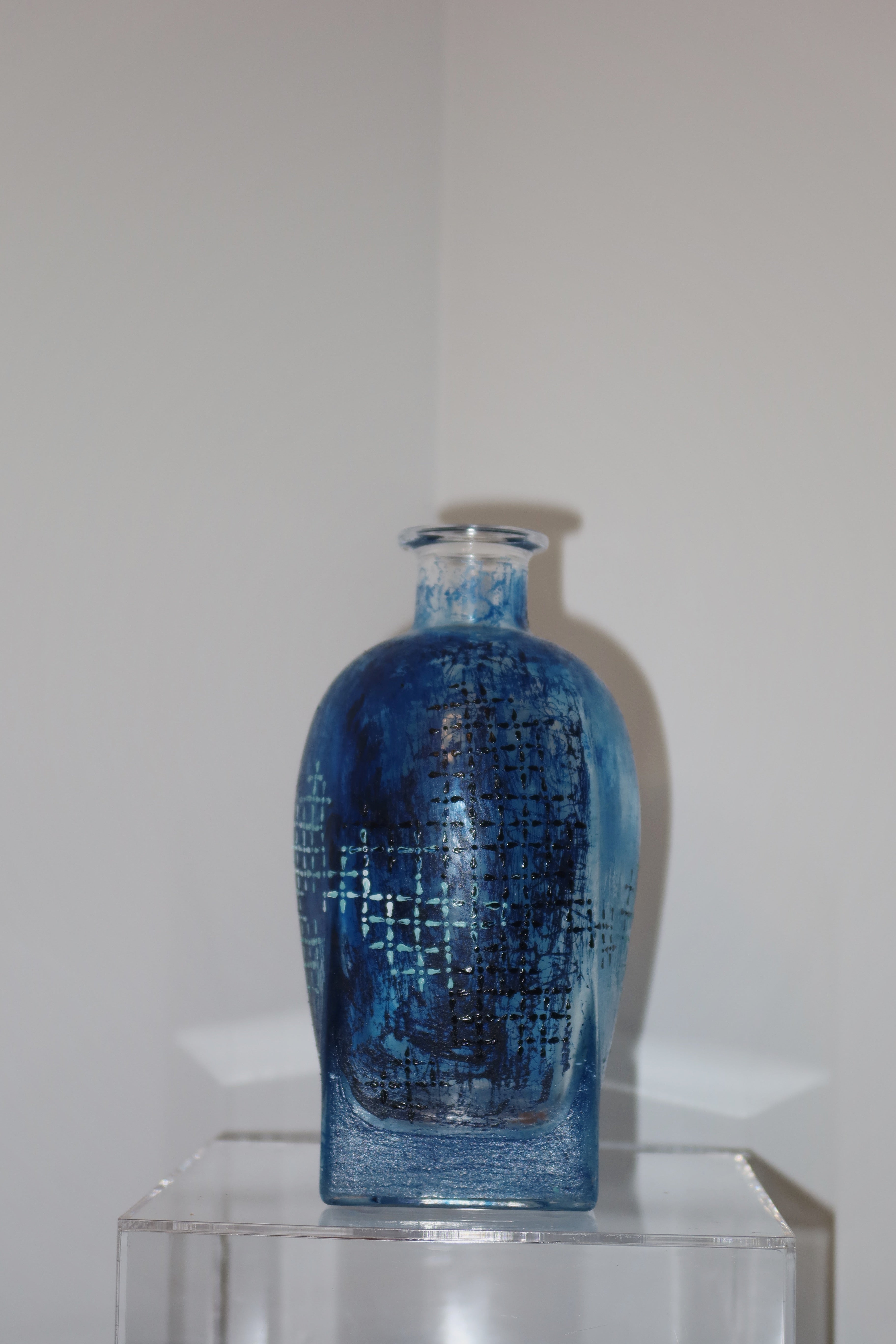 Blue textured glass vase on a clear stand against a white background