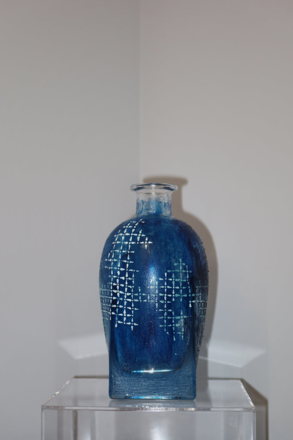 Blue glass vase with geometric pattern on a clear stand against a white background