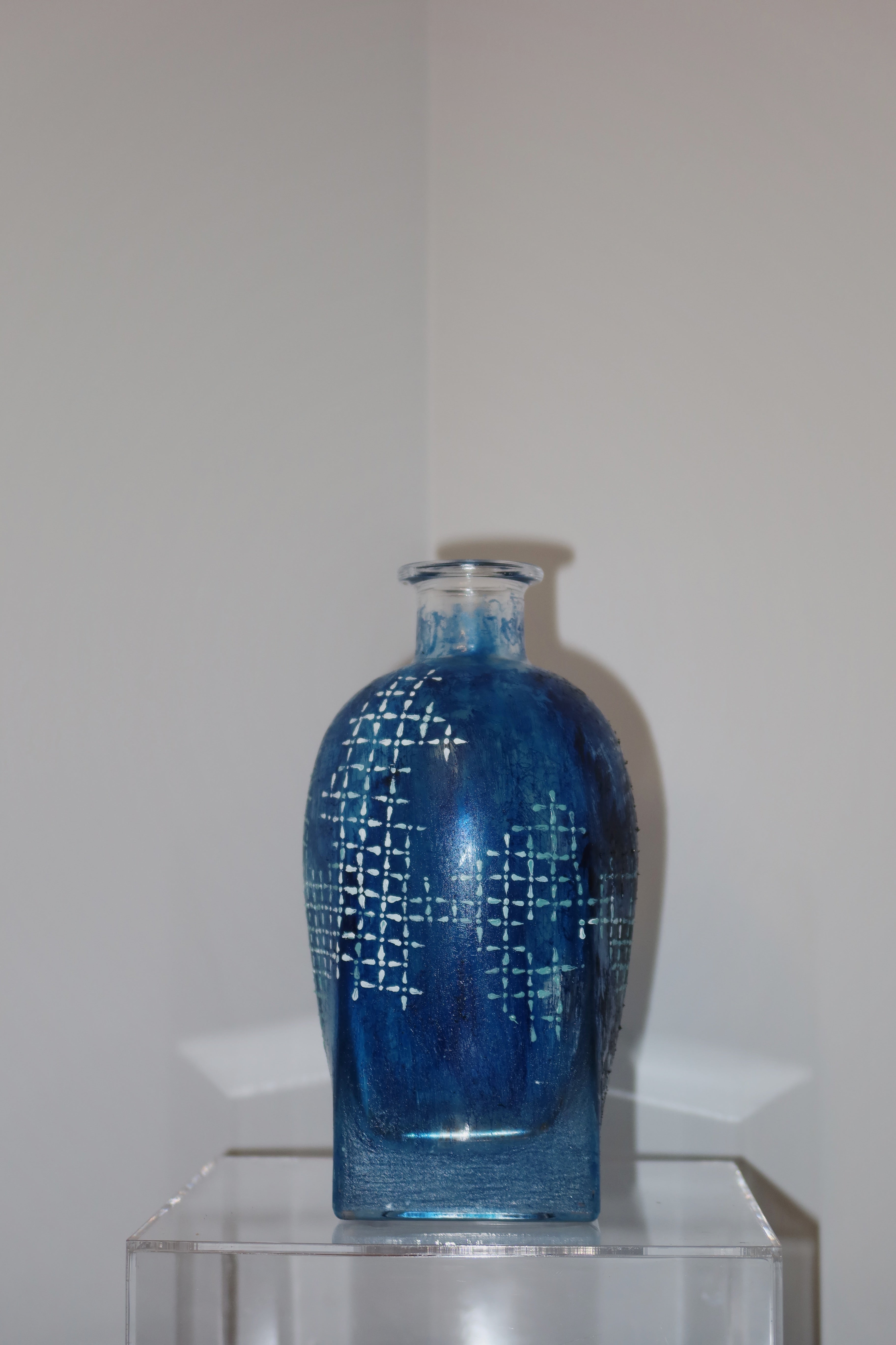 Blue glass vase with geometric pattern on a clear stand against a white background
