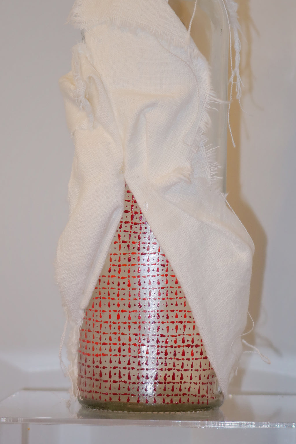 Decorative item wrapped in white fabric with a hand-painted red/orange pattern painted on the glass