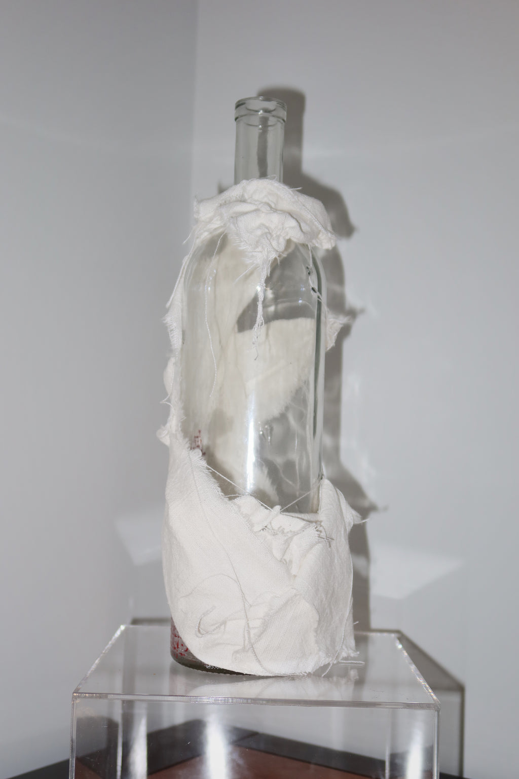 Glass bottle filled with white material on a clear stand against a plain wall
