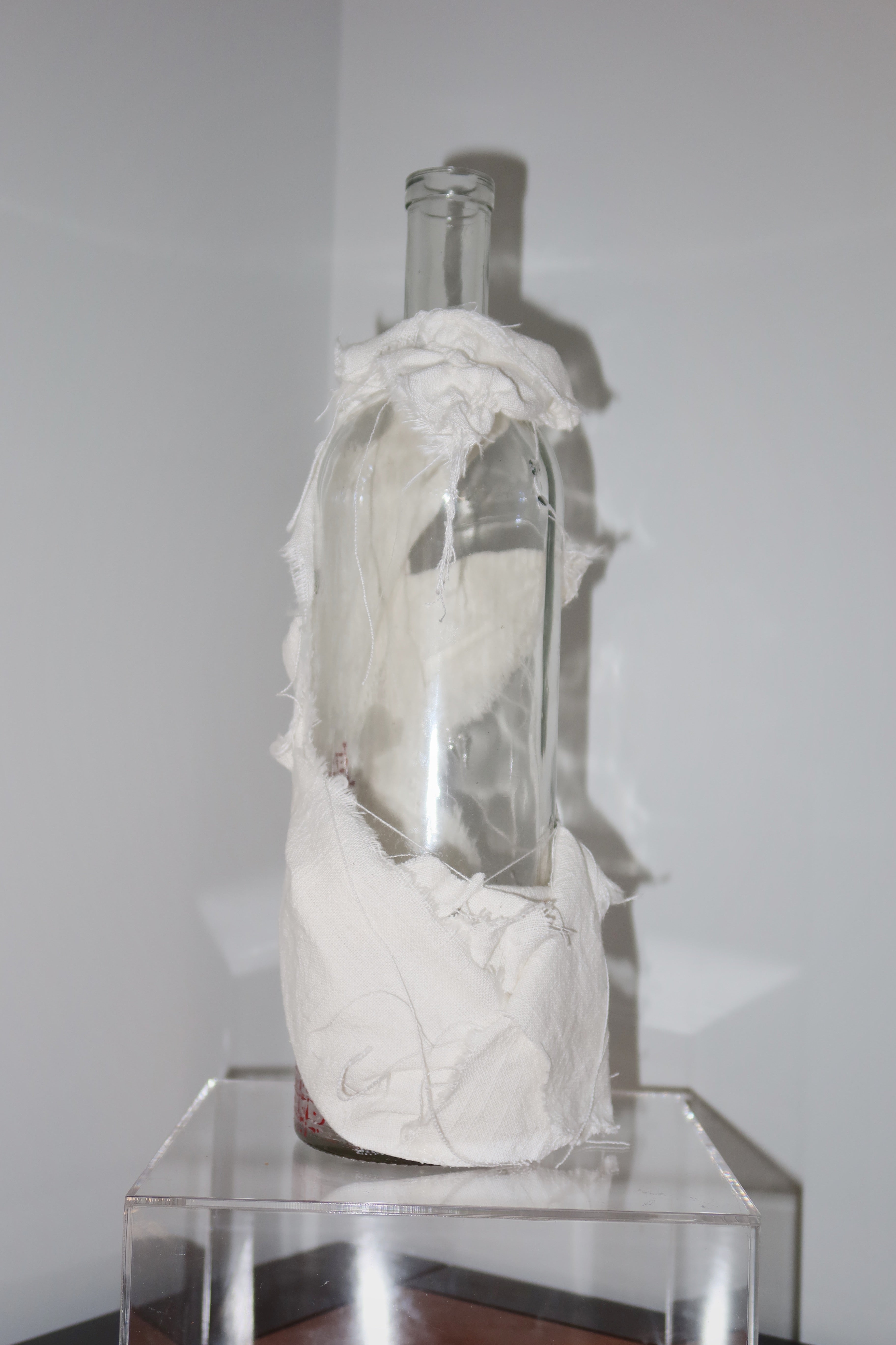 Glass bottle filled with white material on a clear stand against a plain wall