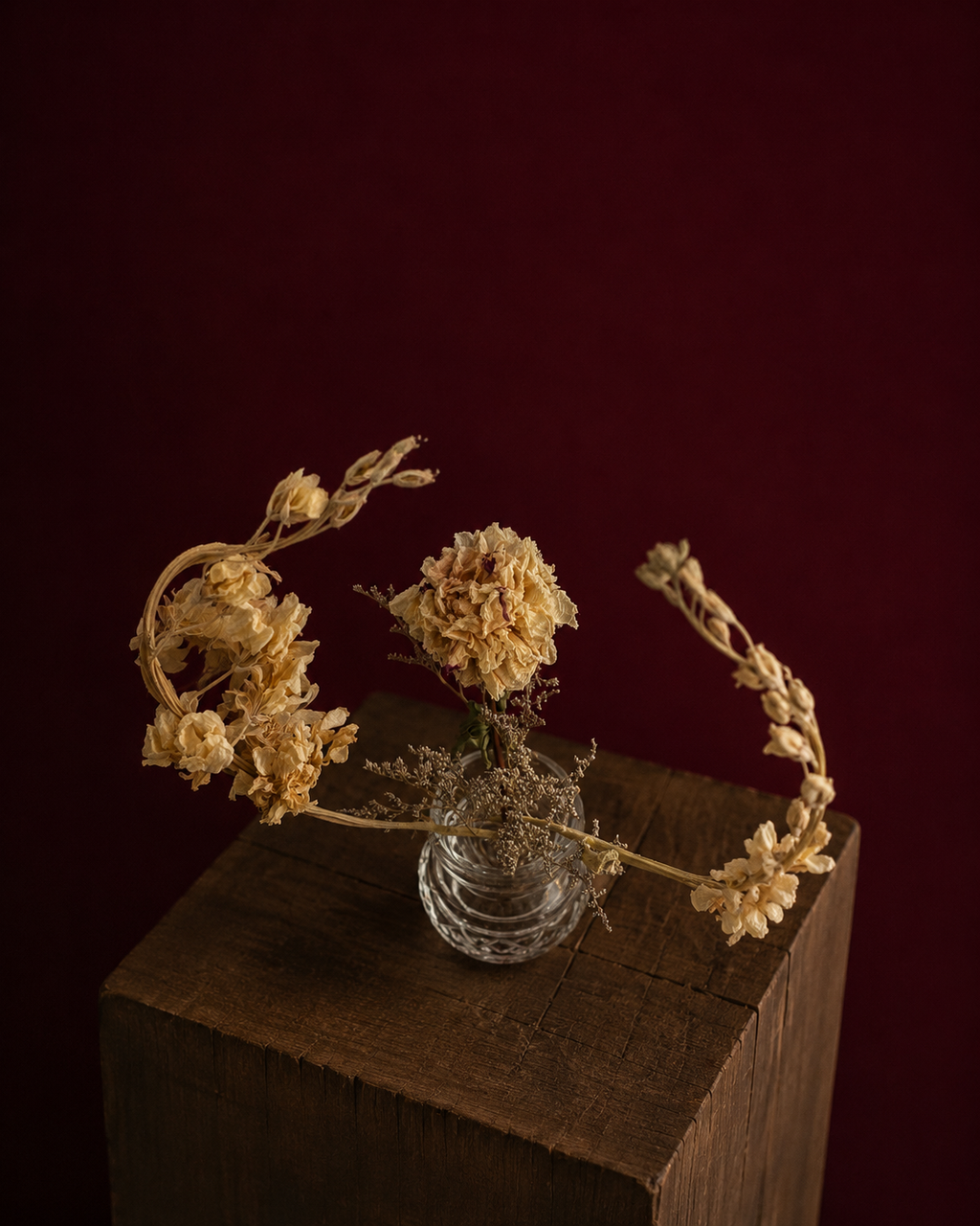 Overhead view of the crystal vase with dried peony and other flowers on a wooden surface against a dark red background
