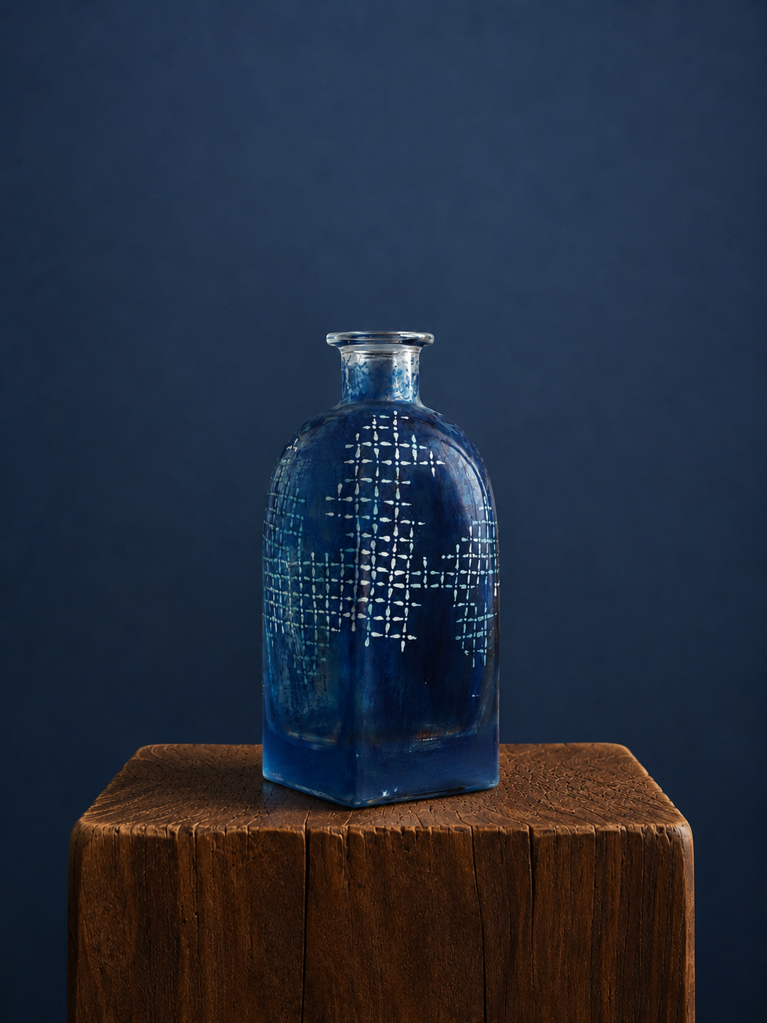 Blue textured bottle, handed painted pattern on blue bottle, sitting on a wooden pedestal against a dark blue background