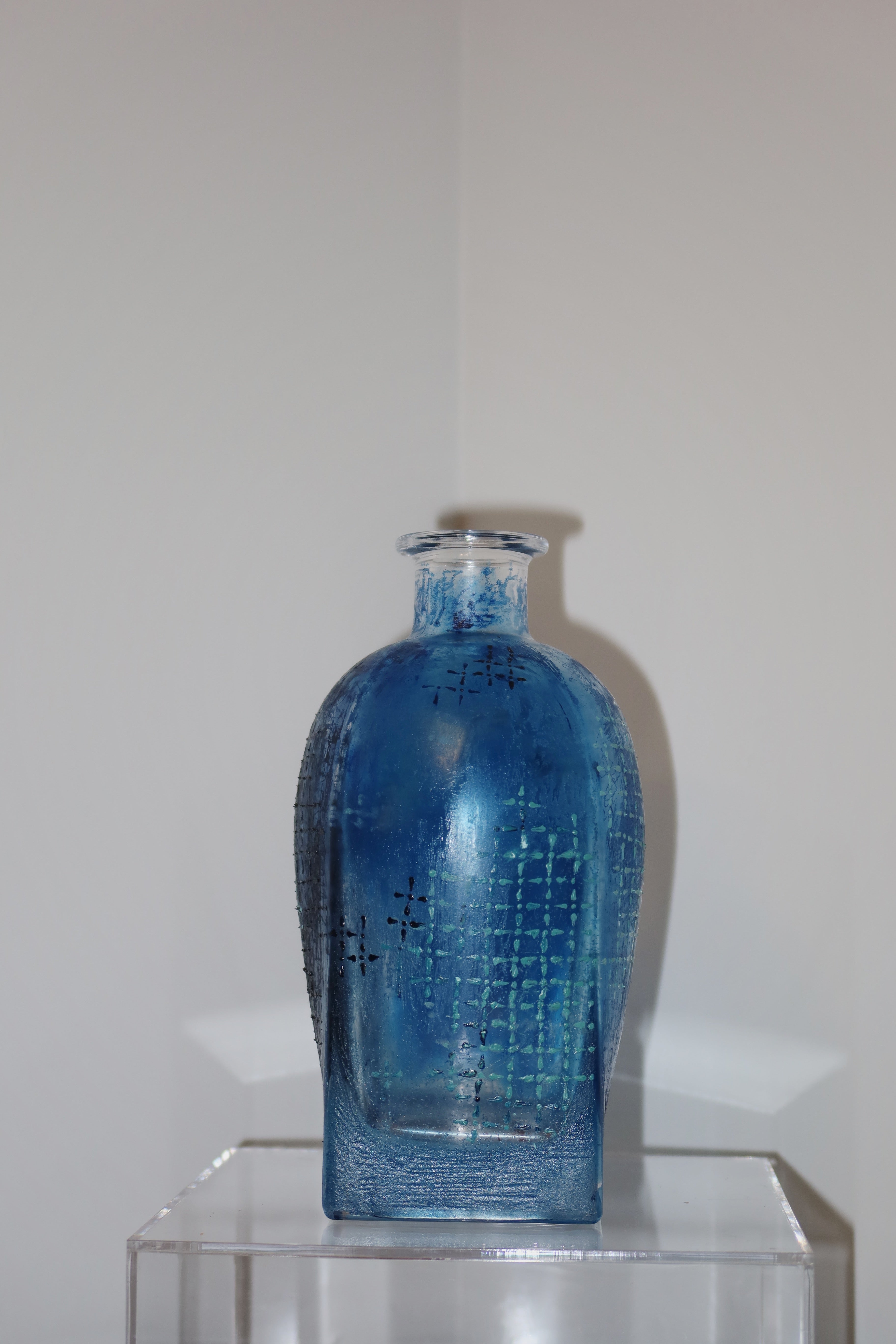 Blue glass bottle with textured surface on a clear stand against a white background