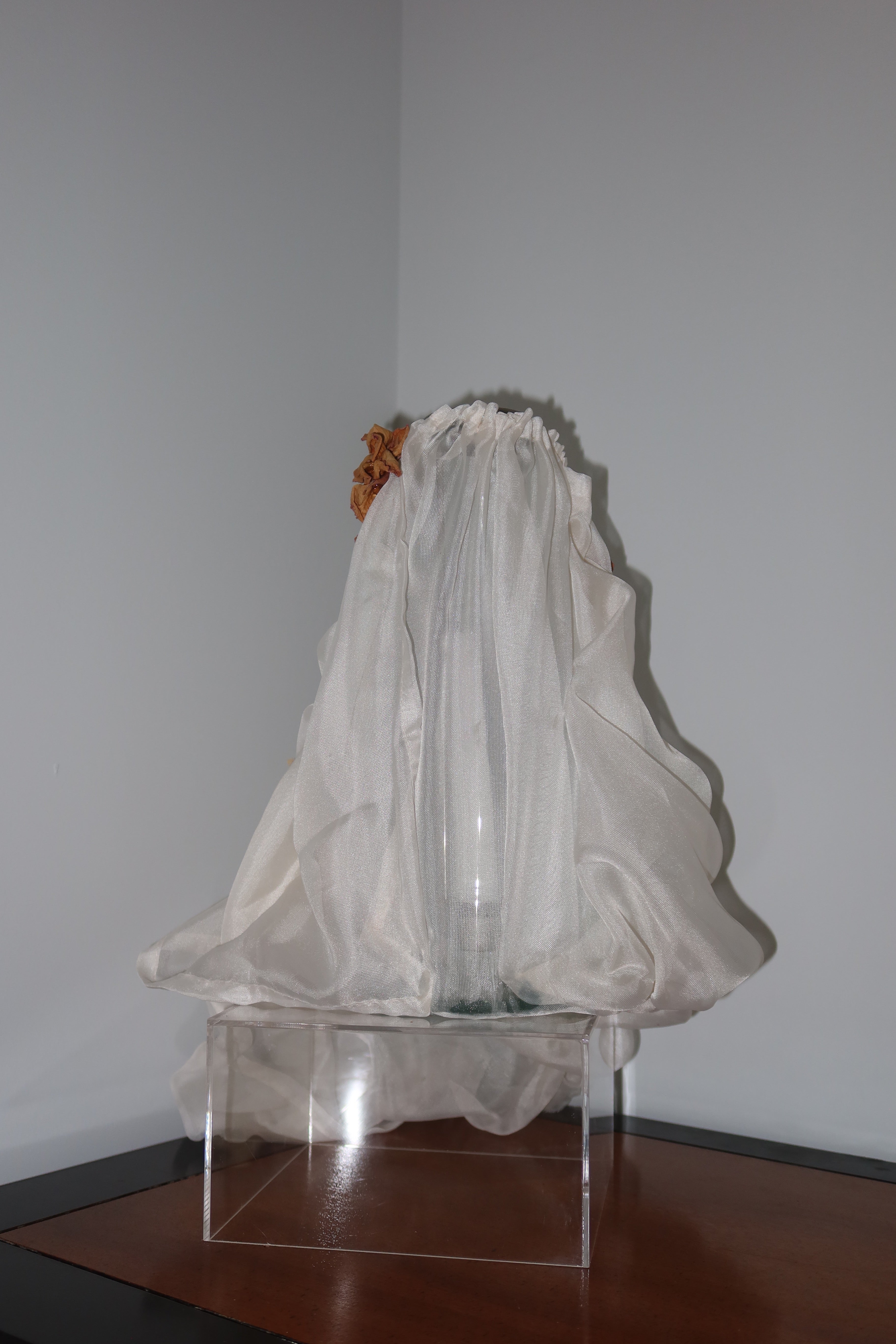 back of candle vase with white mesh fabric draped over it, little roses and baby breath embellishing the light weight cream fabric, standing on a wooden surface against a dark red background