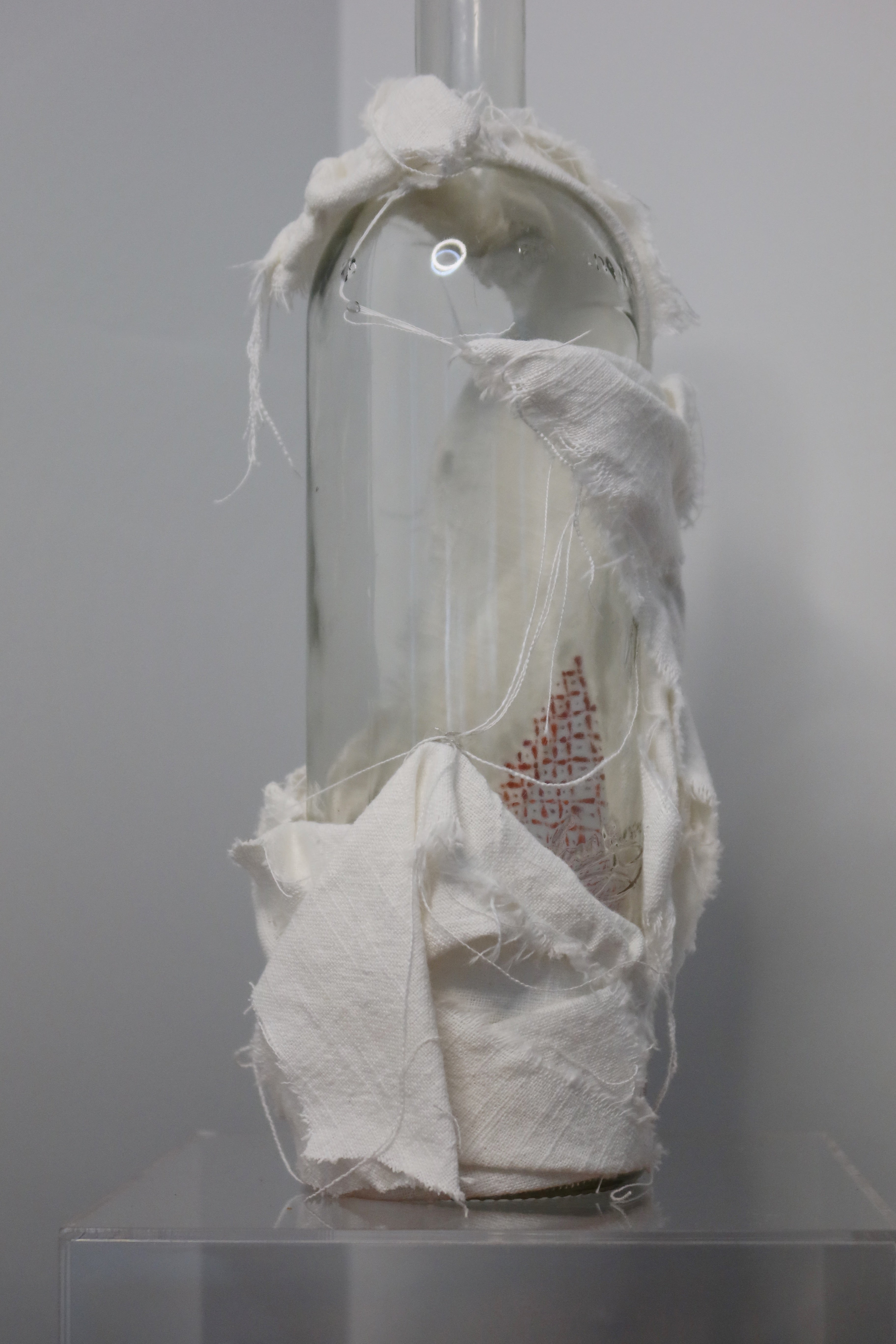 Glass bottle with white linen, hand-painted red pattern, on a white background