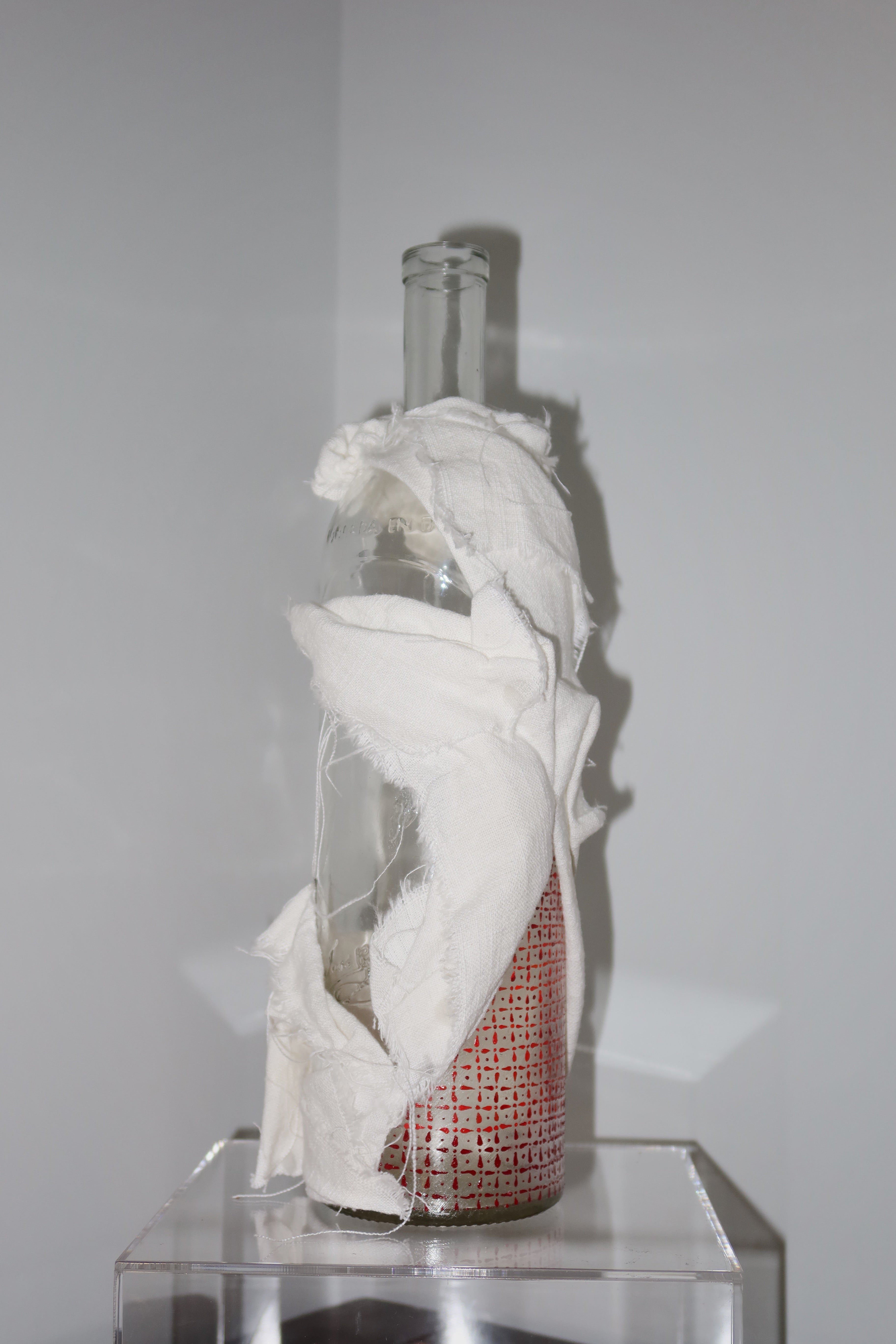 Glass bottle with white linen, hand-painted red pattern painted on glass against a white background