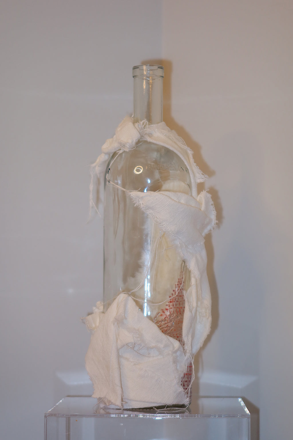 Glass bottle with decorative white linen on a white background.