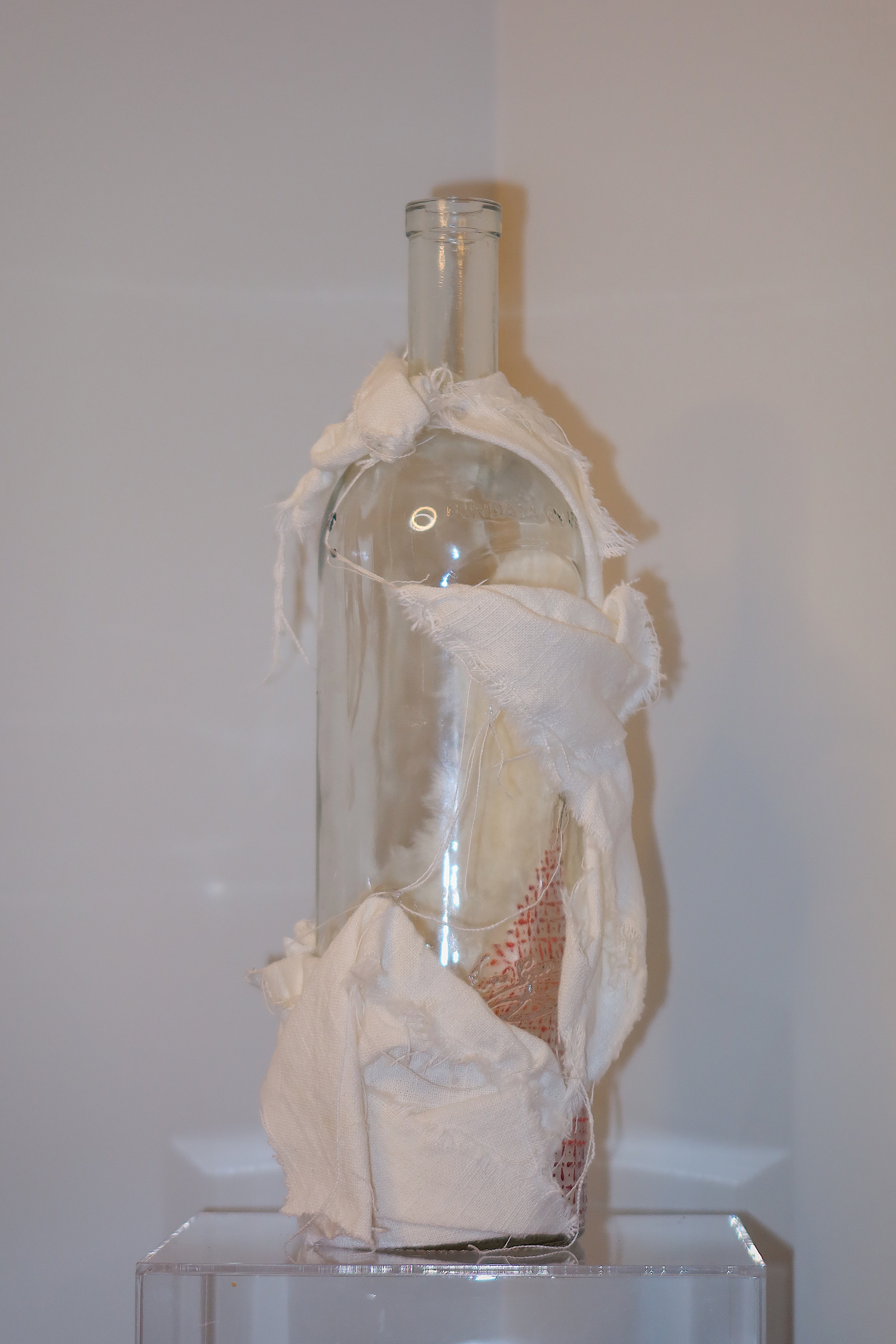 Glass bottle with decorative white linen on a white background.