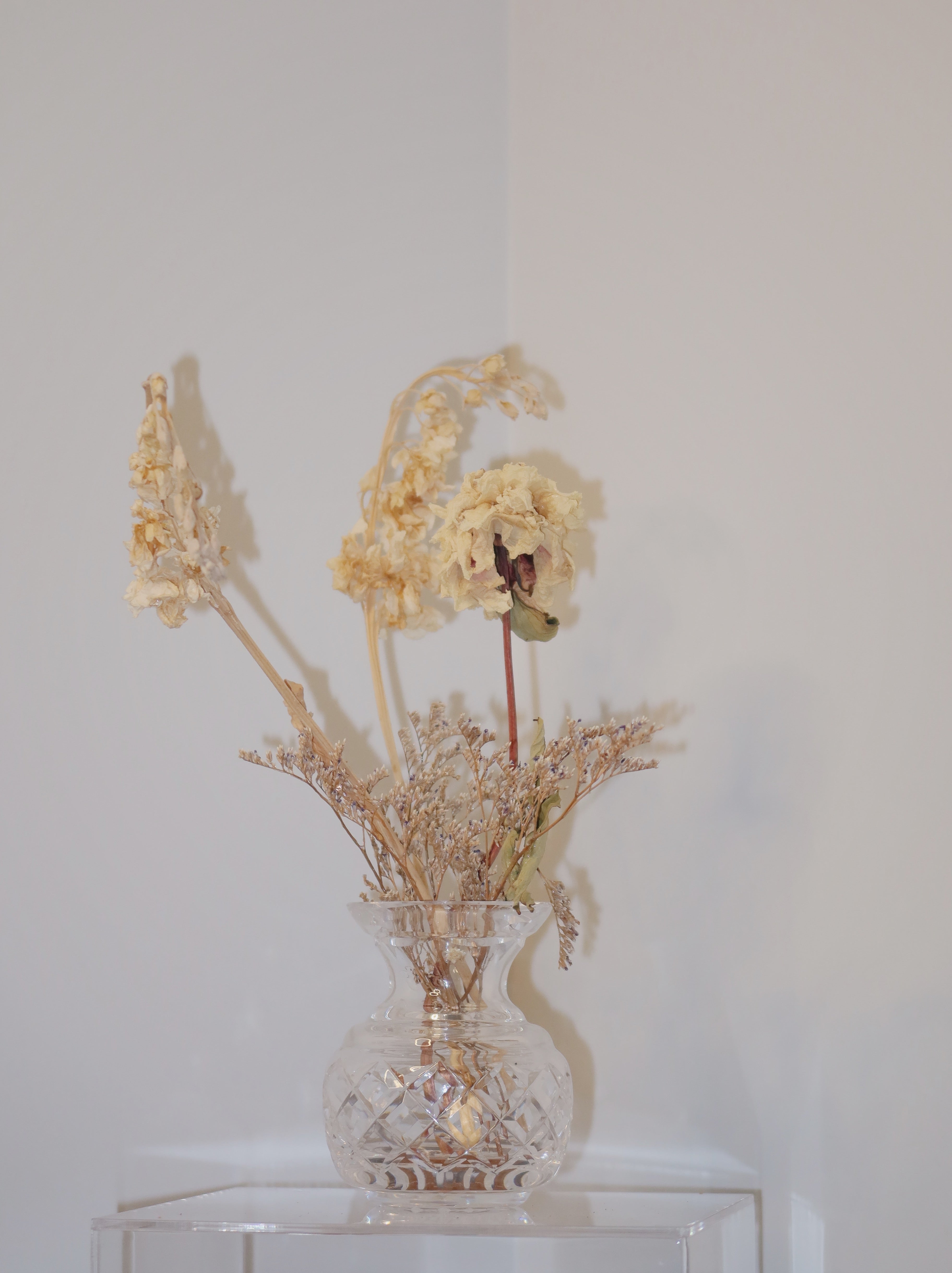 crystal vase with dried peony and other flowers on a clear surface against a white background.