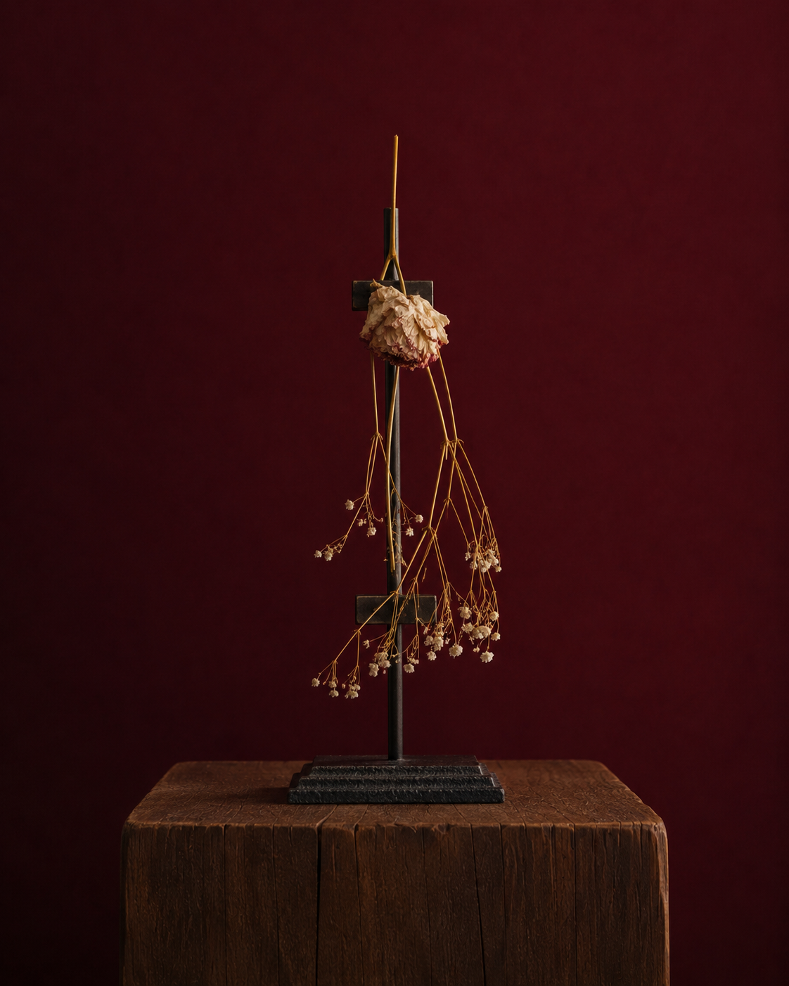 Decorative plant sculpture. A peony standing because of the metal easel supporting in, standing on a wooden pedestal against a dark red background