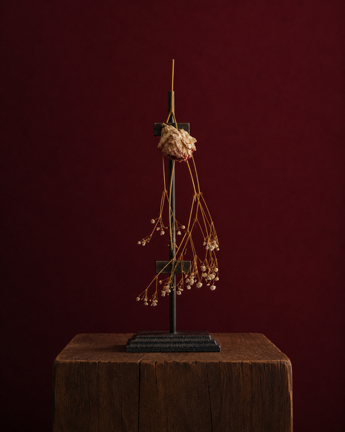 Decorative plant sculpture. A peony standing because of the metal easel supporting in, standing on a wooden pedestal against a dark red background